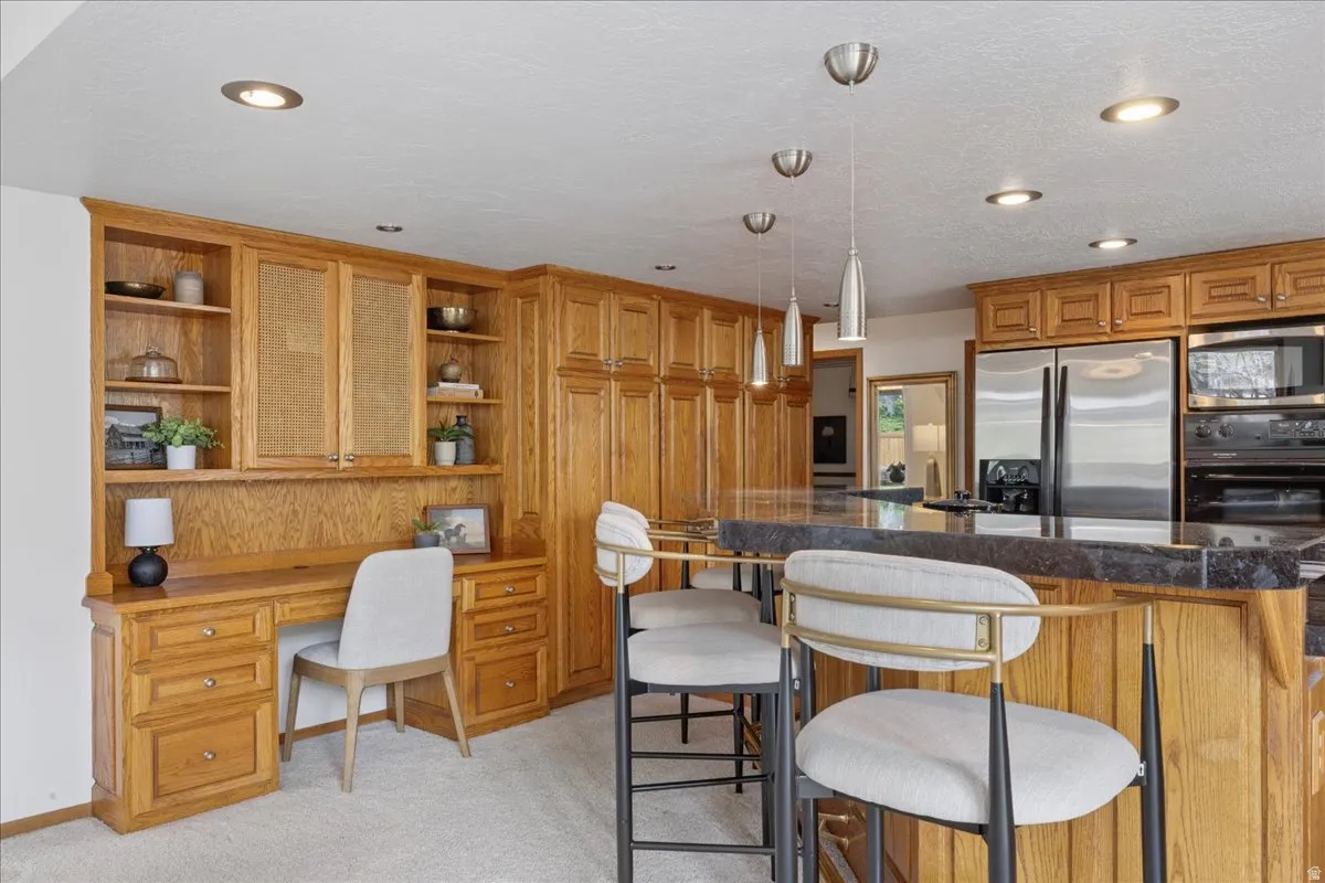 Kitchen featuring extensive wood cabinetry, a built-in desk area, a kitchen island with seating, stainless steel appliances, and recessed lighting