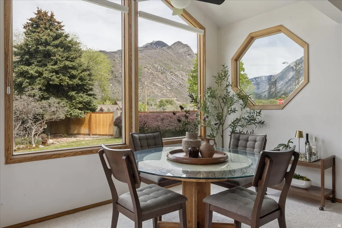 Dining area featuring expansive picture windows with natural wood trim, showcasing a mountainous landscape and mature trees