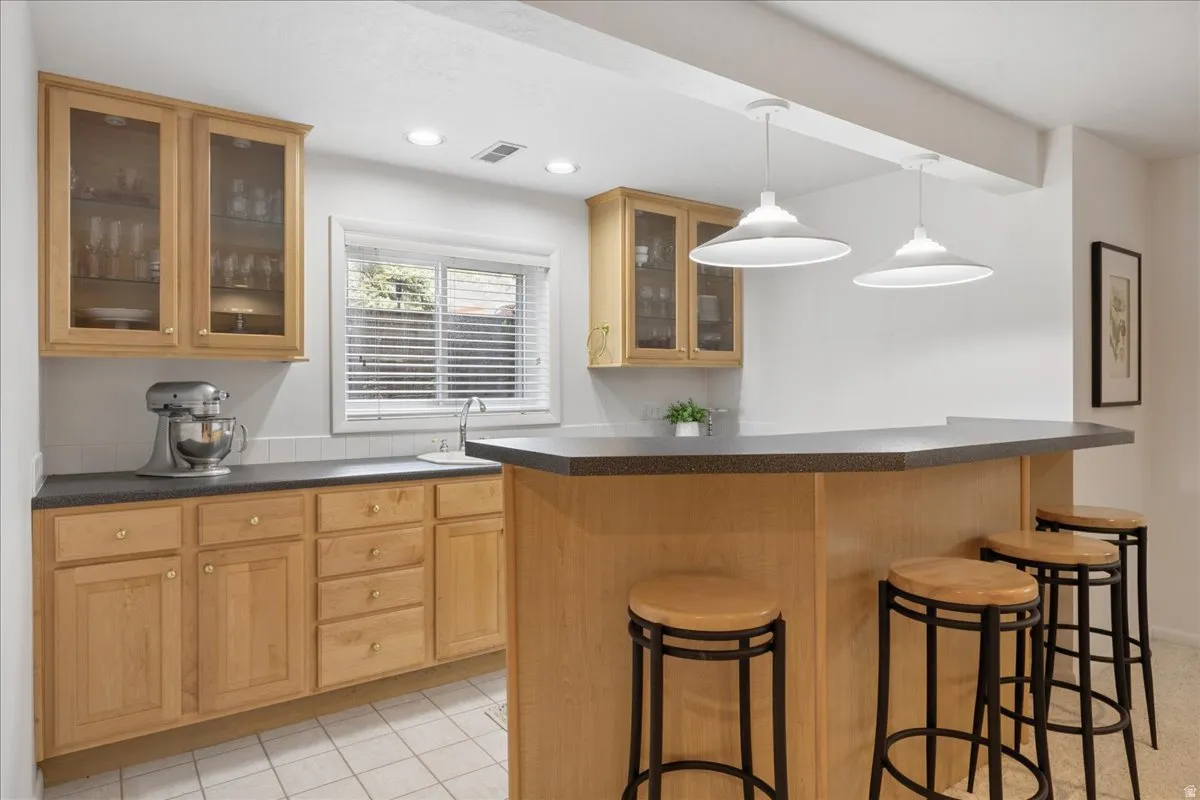 Entertainment bar featuring a dark countertop, light wood-finish cabinetry, and recessed lighting