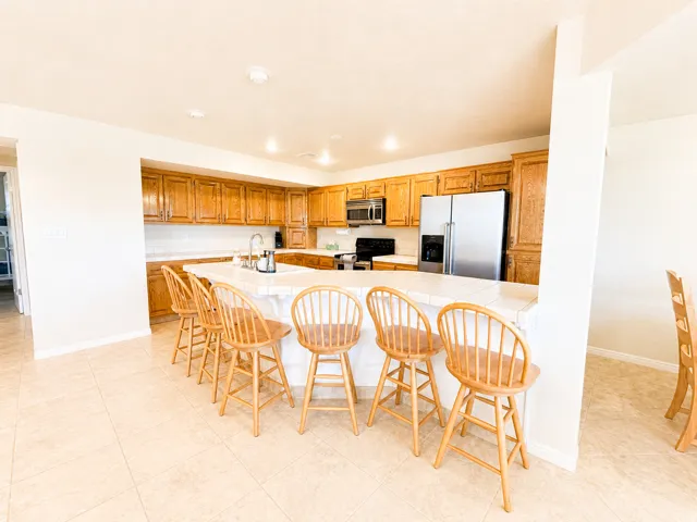 Kitchen featuring a large tiled island with seating, extensive wood cabinetry, and stainless steel appliances including a refrigerator and oven