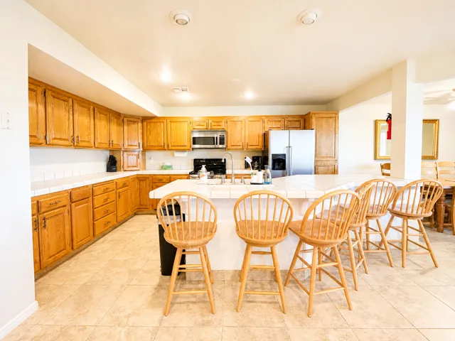 Open-concept kitchen featuring light wood cabinetry, white tiled countertops, and a central island with a tiled breakfast bar