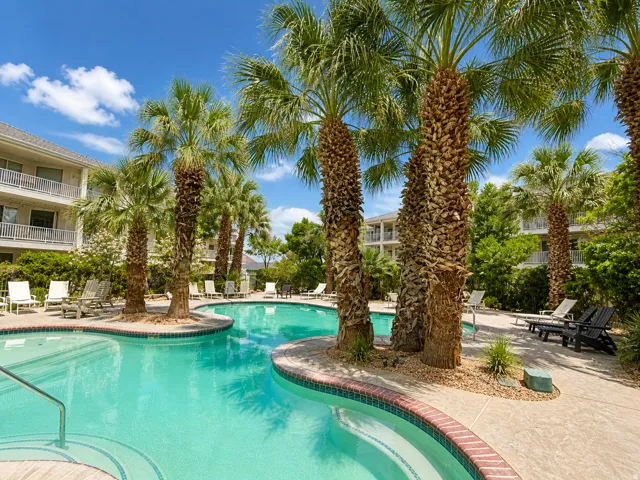 Curved swimming pool featuring a tiled interior, a red brick coping, and a surrounding concrete patio
