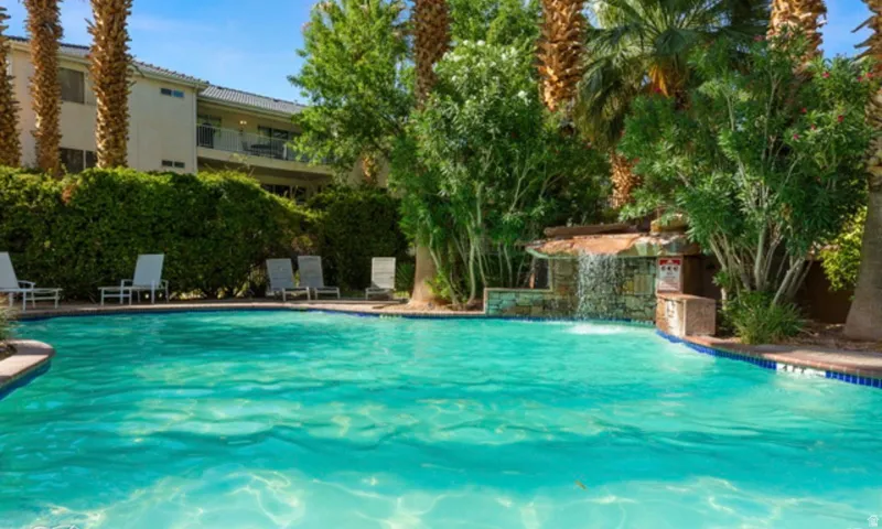 Resort-style pool area featuring a rock waterfall, lush landscaping, and mature palm trees