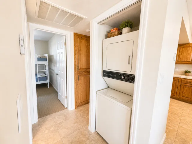 Hallway with tile flooring, featuring a stacked washer and dryer unit, an adjacent built-in wood-finish cabinet, and a visible doorway to a carpeted interior space