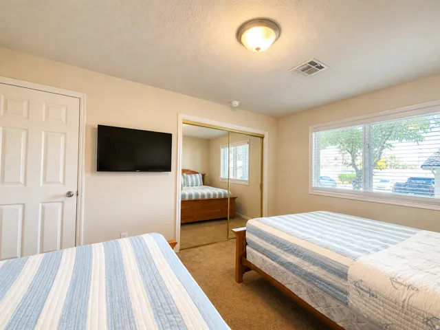 Carpeted room featuring a white paneled door, wall-mounted television, and a window with blinds