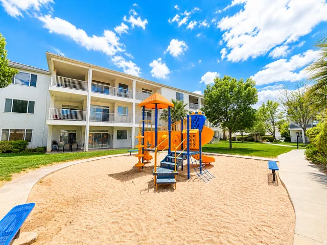 Outdoor play area featuring a sand base and a colorful play structure with slides and climbing elements