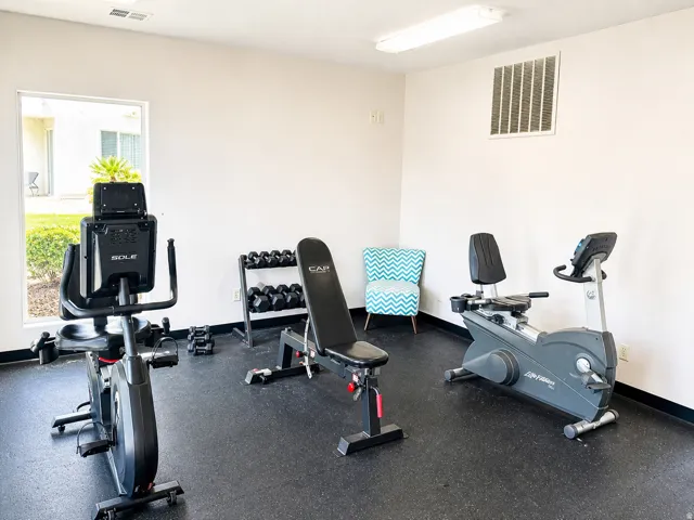 Fitness area featuring rubber flooring, a stationary bike, a recumbent bike, and a dumbbell rack