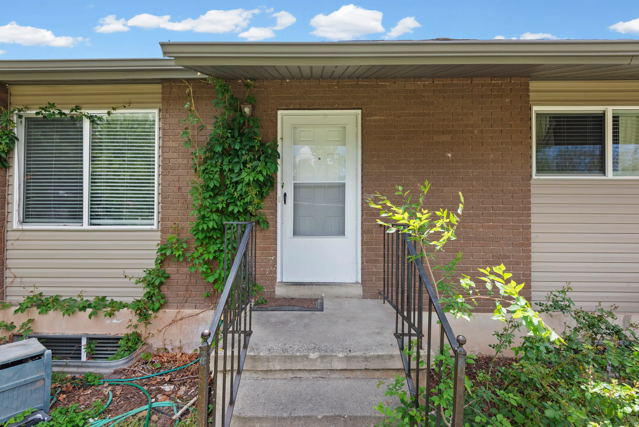 Entryway featuring a white storm door, concrete steps, and black metal handrails