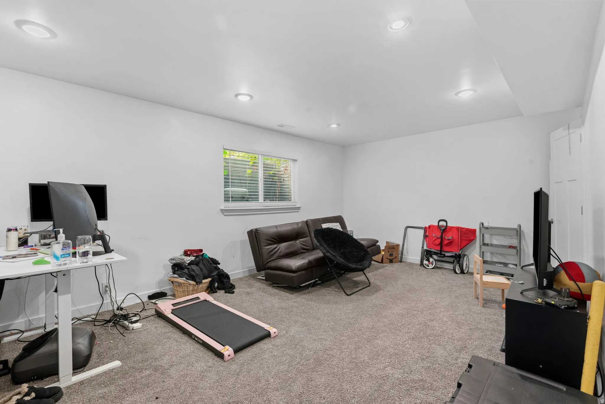 Spacious carpeted room featuring recessed lighting, a window with horizontal blinds, and a built-in storage cabinet