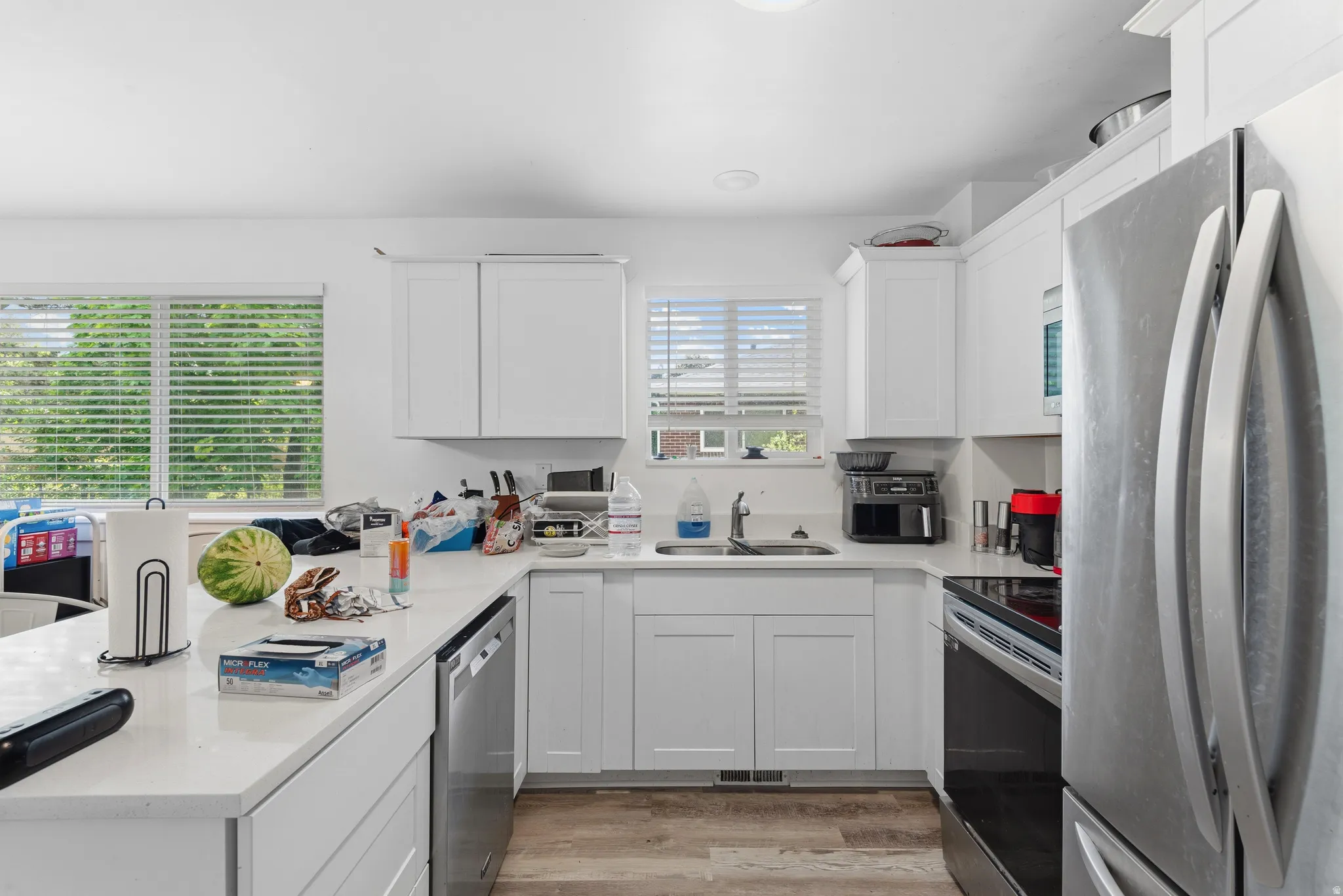 Bright kitchen featuring white shaker cabinetry, light countertops, stainless steel appliances, and wood-finish flooring
