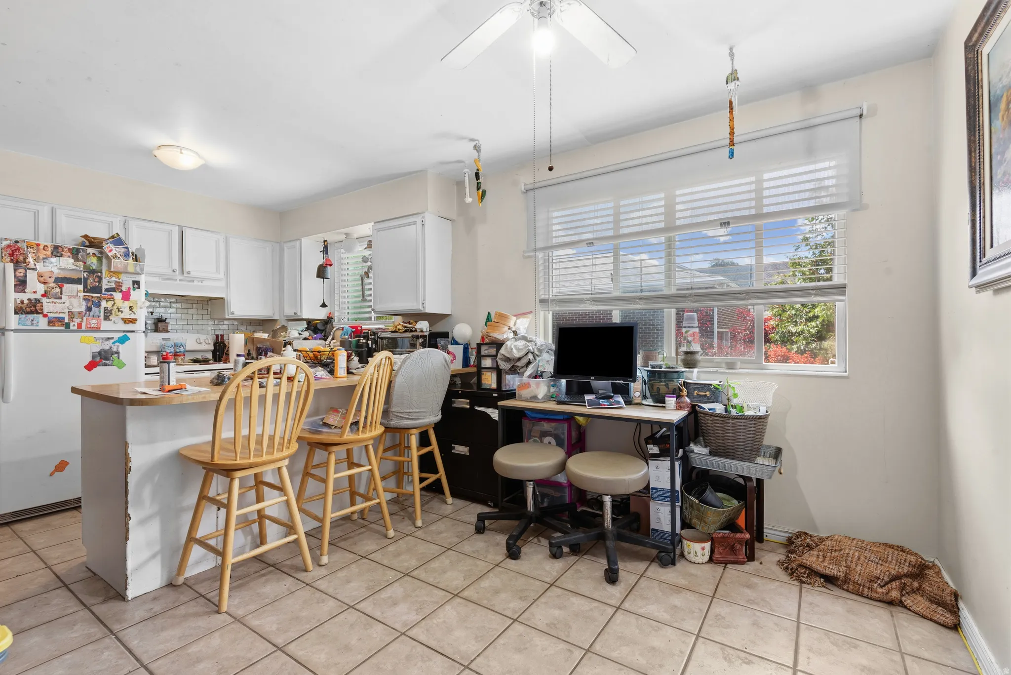 Kitchen featuring tile flooring, white cabinetry, a built-in breakfast bar, and a window with horizontal blinds