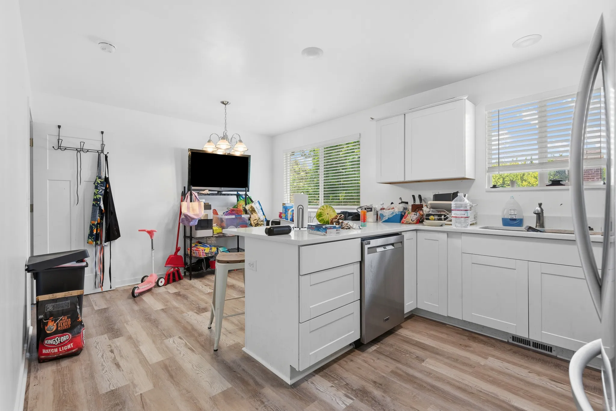 Modern kitchen featuring white cabinetry, light-toned wood-finish flooring, and two windows with blinds