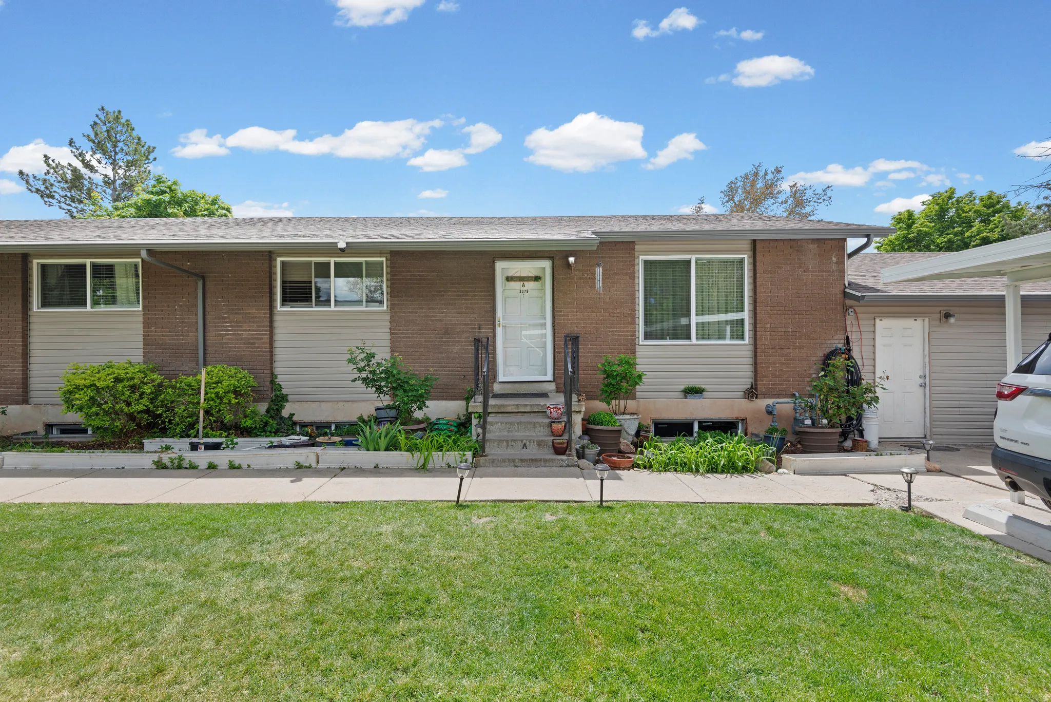 Brick exterior with complementary siding, a covered entry, established landscaping, and a carport