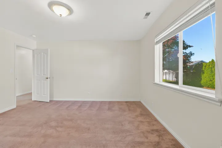 Spacious room featuring neutral painted walls, light brown carpeting, a large window with white blinds, and a white interior door with a paneled design