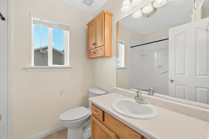Bathroom featuring a light-colored vanity with an integrated sink, a large wall-mounted mirror, and a window with blinds