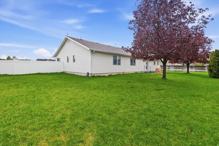 Expansive backyard featuring a manicured lawn, a full-height privacy fence, and mature trees with blossoming foliage