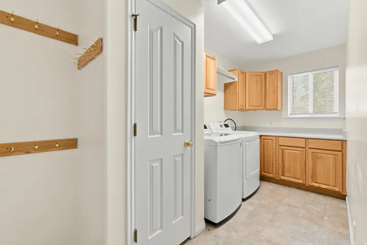 Dedicated utility room featuring light wood cabinetry, stone-finish countertops, and a window for natural illumination