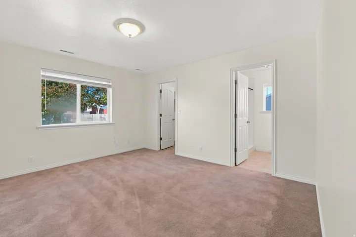 Spacious room featuring neutral carpeting, light-toned walls, and a large window with horizontal blinds