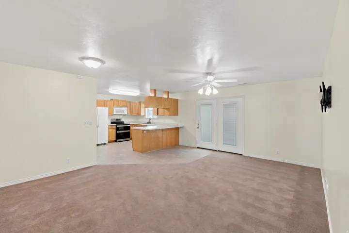 Open-concept living area featuring a neutral carpet, ceiling fan, and French doors with internal blinds