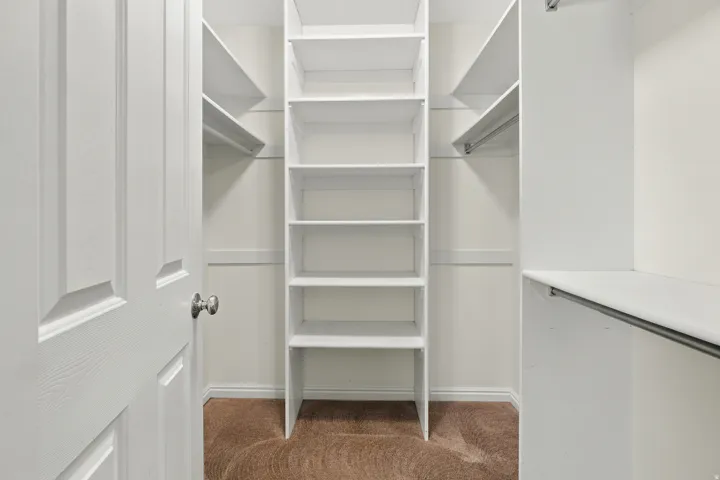 Walk-in closet featuring built-in shelving, hanging rods, and light brown carpeting