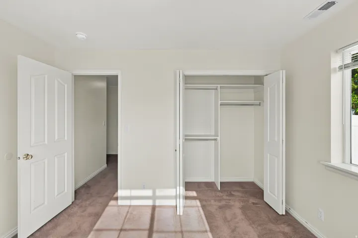 Room featuring a built-in closet with bifold doors, an open doorway, and a window with blinds