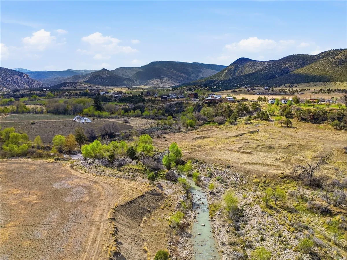 Expansive natural landscape featuring a winding river, mature trees, open fields, and distant mountainous terrain