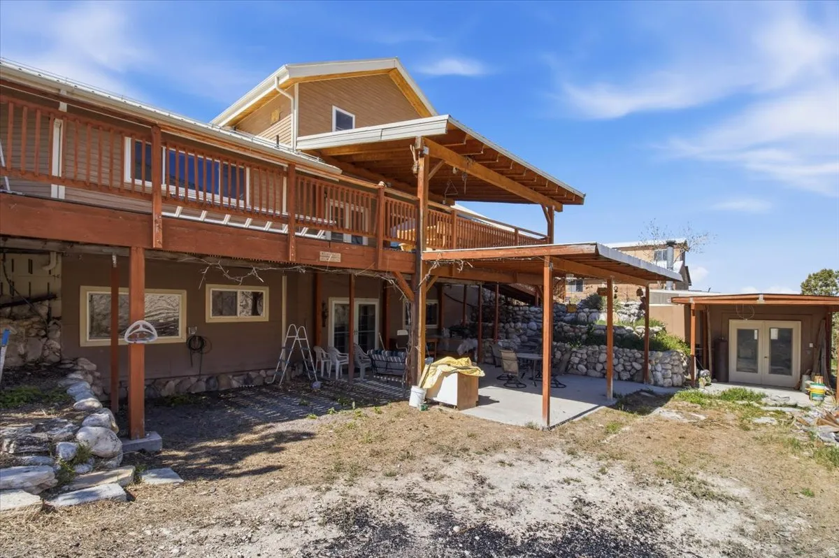 Multi-level residence featuring an expansive upper deck with wood railing, a covered lower patio, and a separate detached outbuilding with double doors