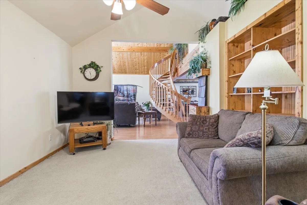 Vaulted ceiling living area featuring a built-in wood bookshelf, light-toned carpeting, and a visible wood spiral staircase