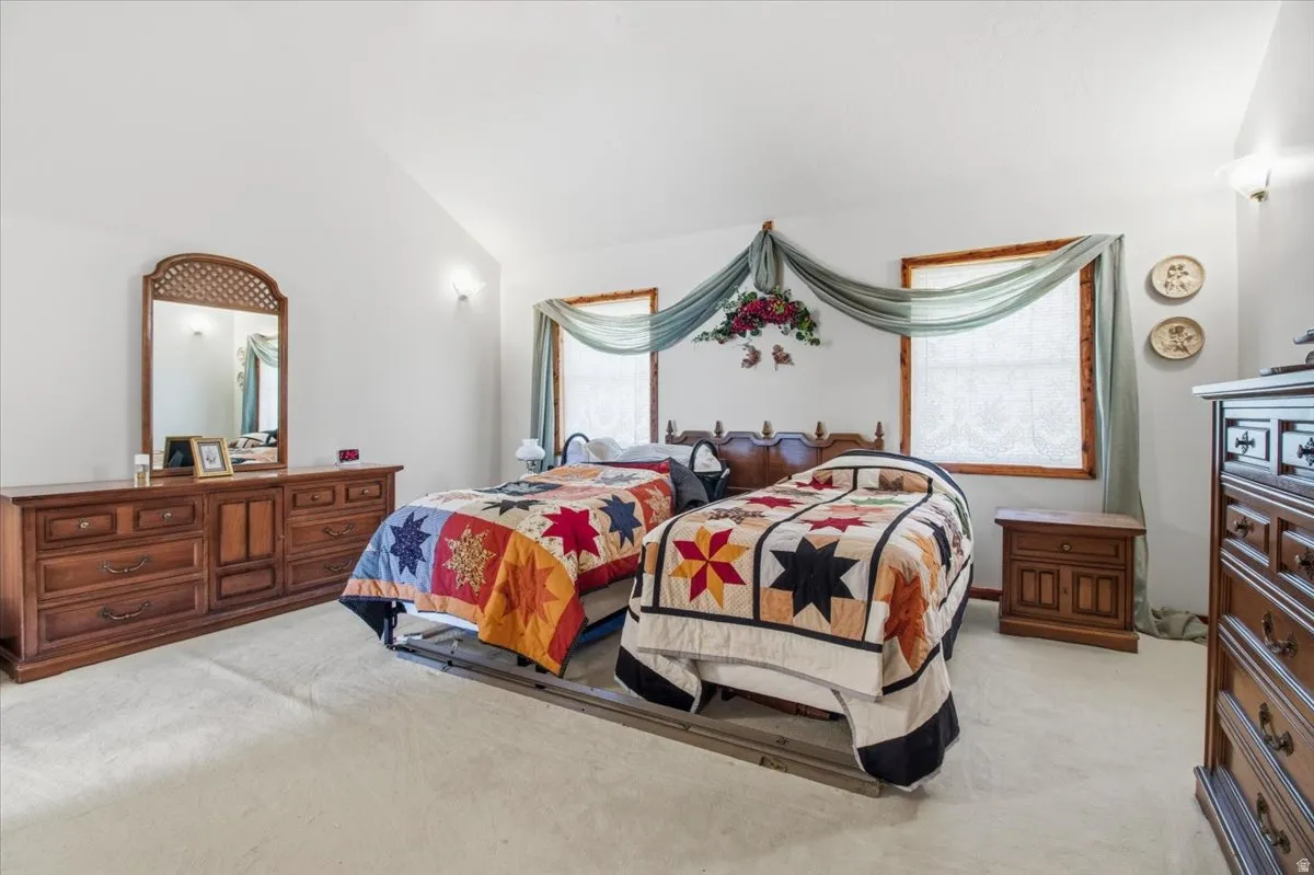 Spacious room featuring vaulted ceilings, light-toned carpeting, and multiple windows with wood trim