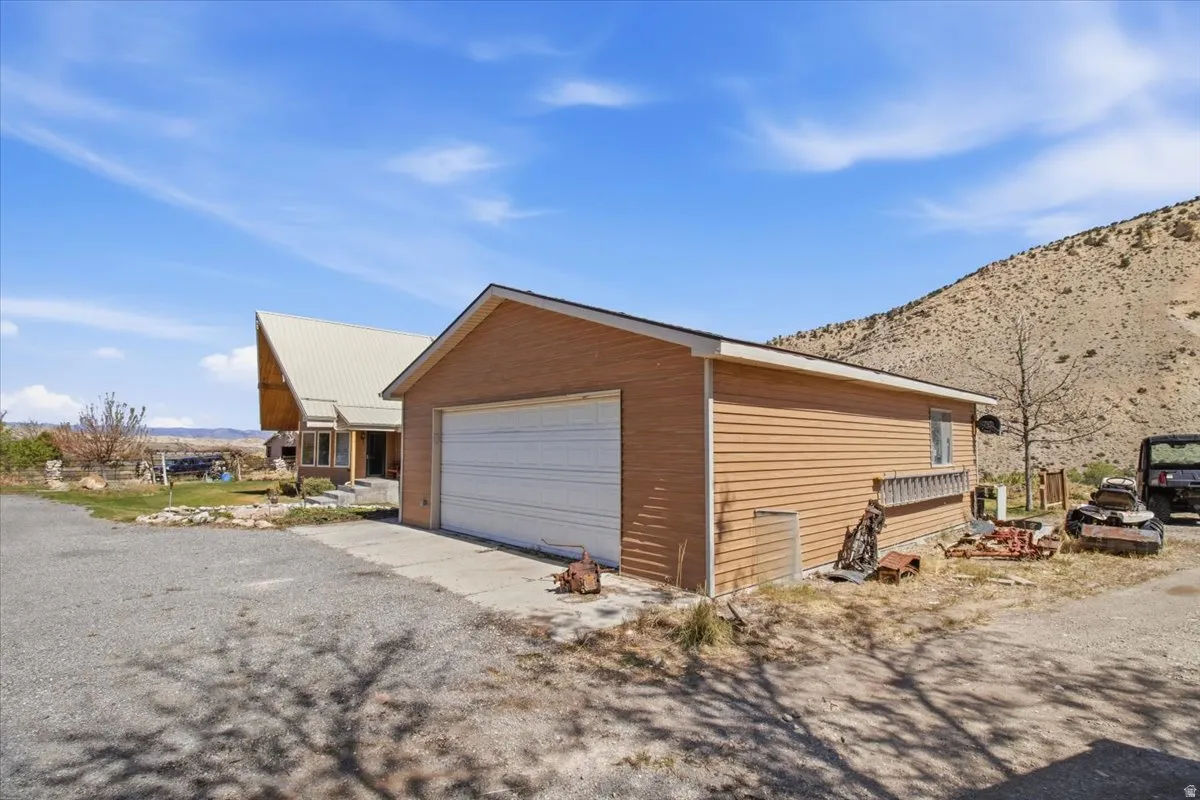 Detached garage with a white overhead door and tan siding, featuring a concrete driveway and gravel parking area
