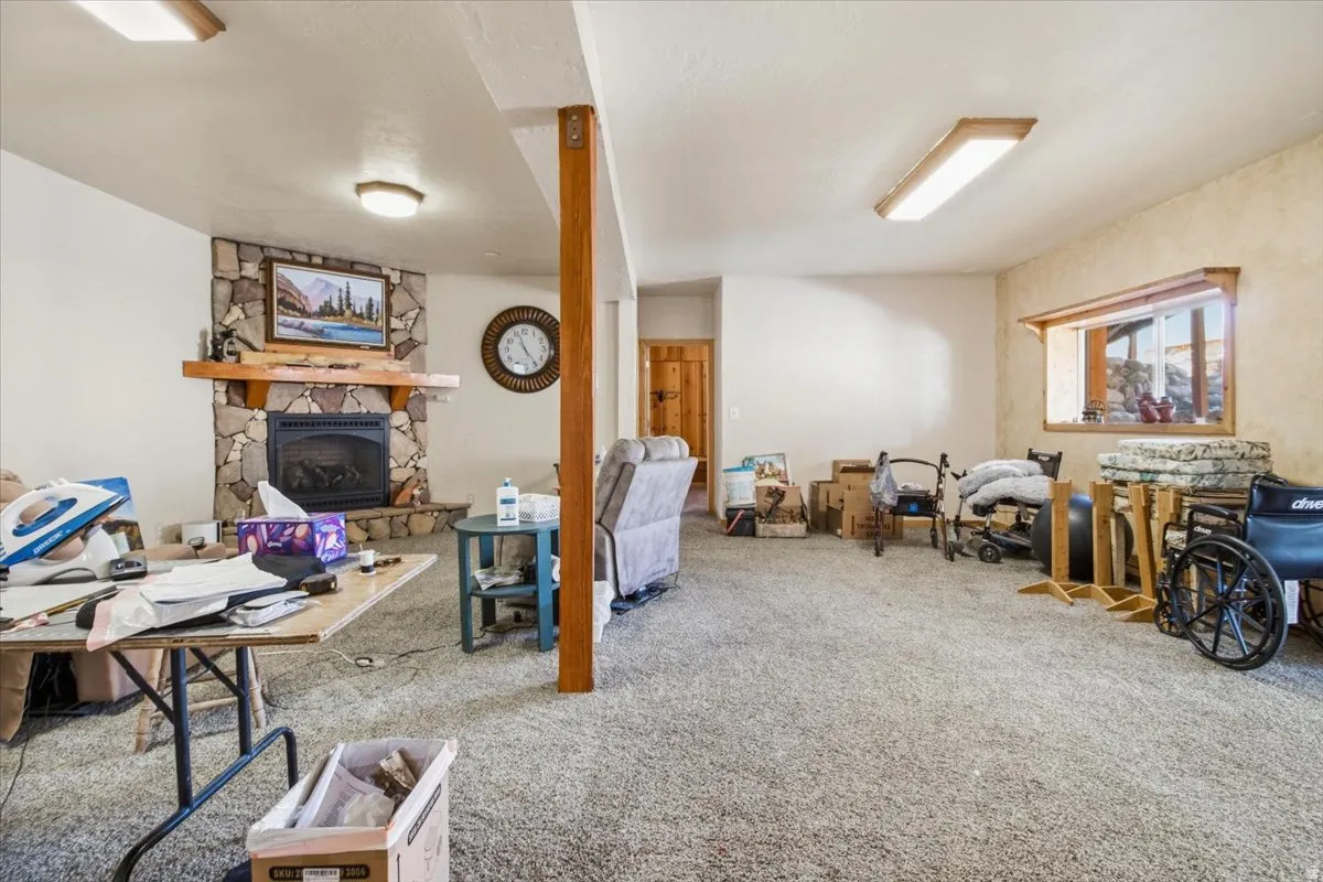 Spacious lower-level room featuring a stone-faced fireplace with a wood mantle, recessed lighting, and a wood-framed window
