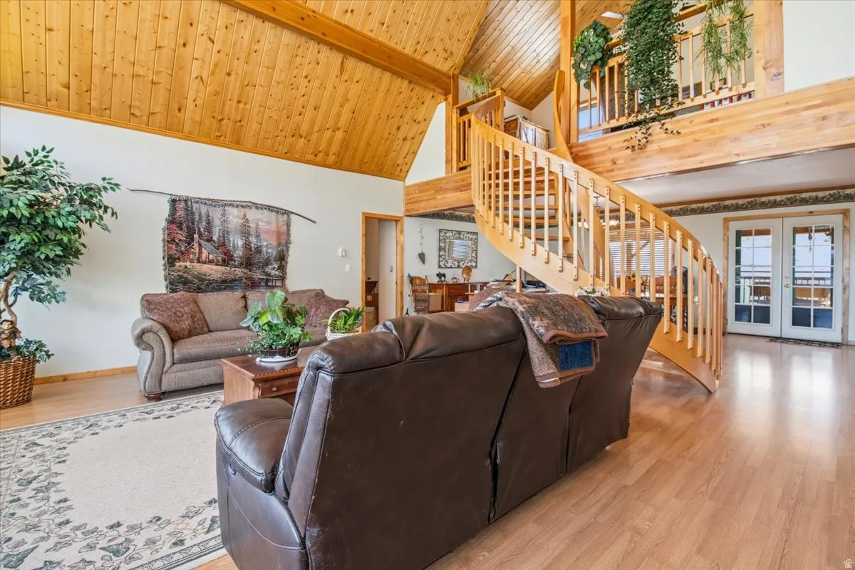 Spacious living area featuring a prominent wood spiral staircase, wood-finish flooring, vaulted wood plank ceiling with exposed beams, and double French doors