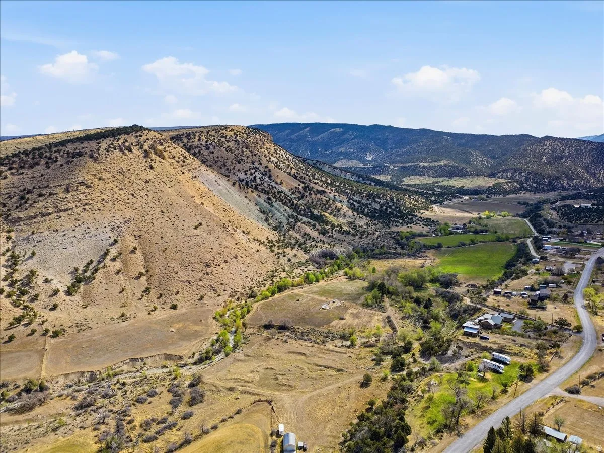Expansive rural landscape featuring a winding road, scattered residential structures, and a prominent mountainous backdrop