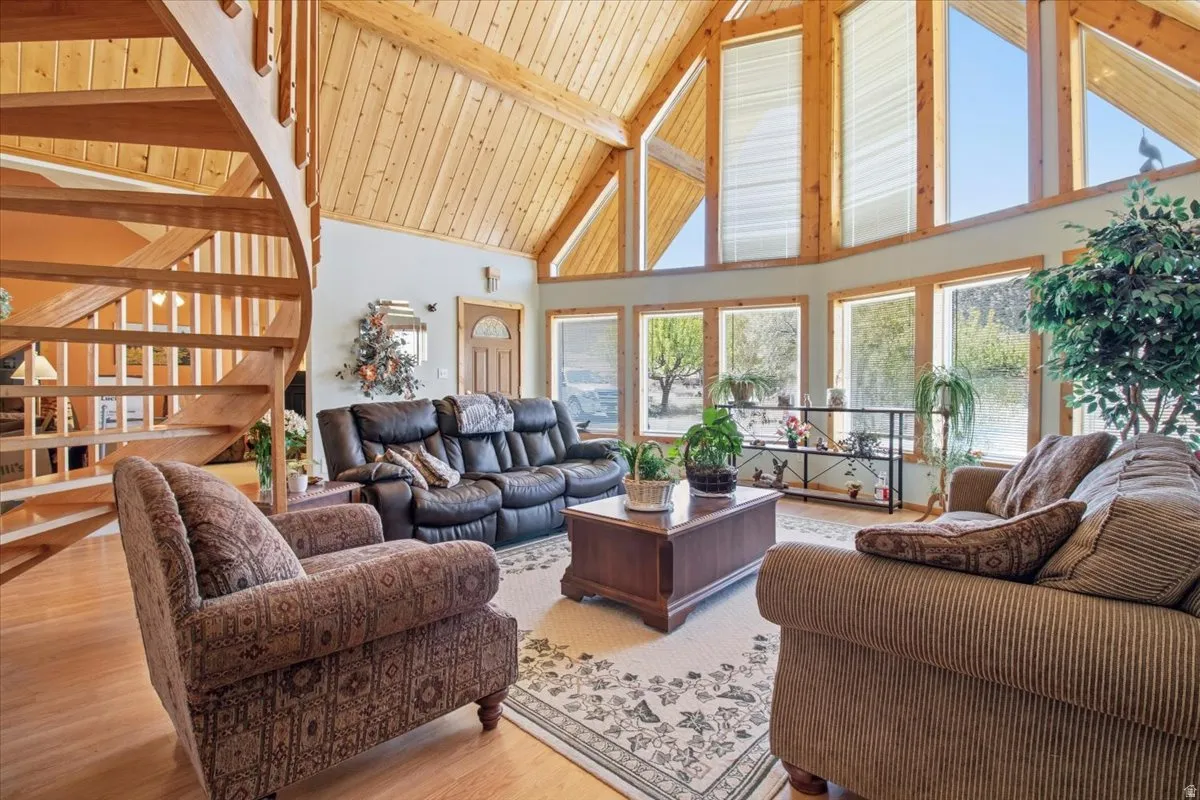 Spacious living area featuring a prominent wood spiral staircase, vaulted wood-plank ceilings, expansive fenestration with transom windows, wood-finish flooring, and light-toned wall finishes