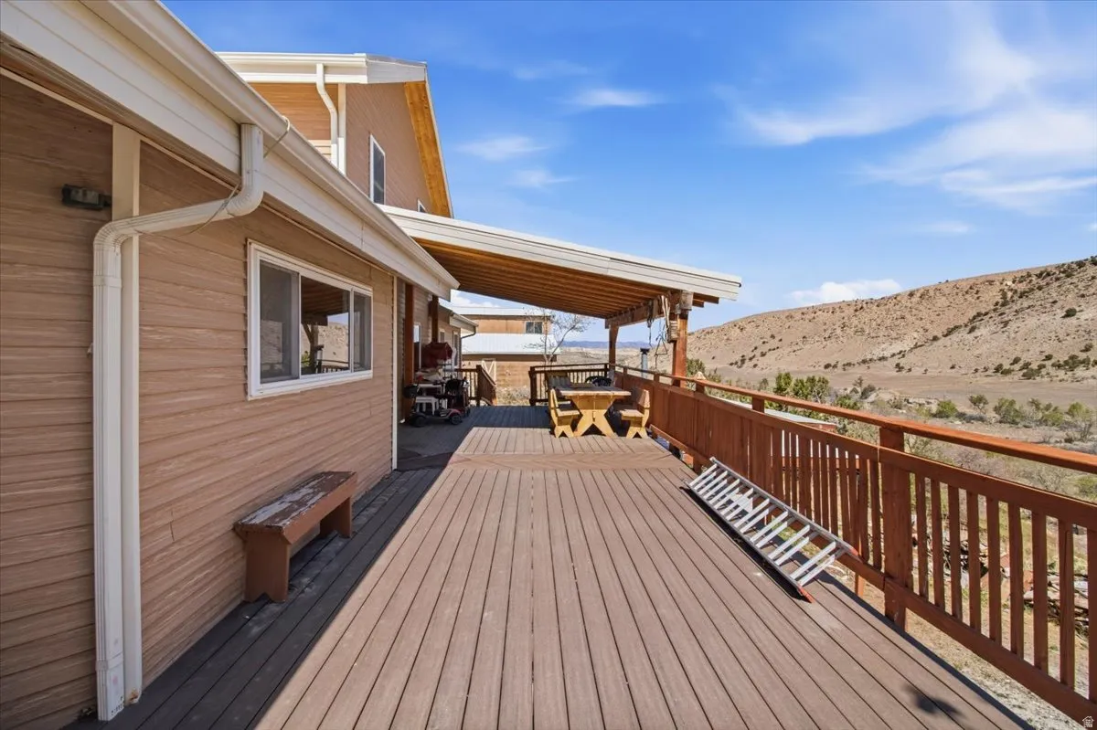 Expansive exterior deck featuring durable wood-finish flooring, a covered patio area, and a wood railing system