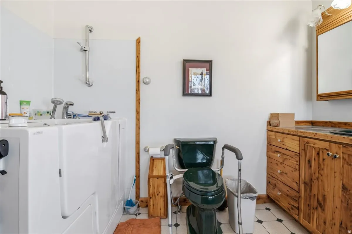 Bathroom featuring a walk-in bathtub with integrated shower, wood-finish vanity with a single sink, tiled flooring, and a mirrored medicine cabinet