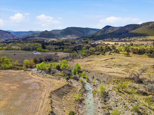 Expansive natural landscape featuring a winding river, mature trees, open fields, and distant mountainous terrain