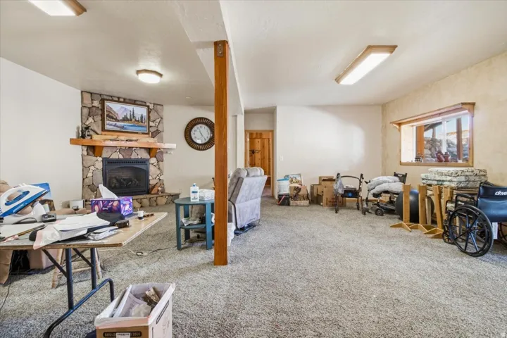 Spacious lower-level room featuring a stone-faced fireplace with a wood mantle, recessed lighting, and a wood-framed window