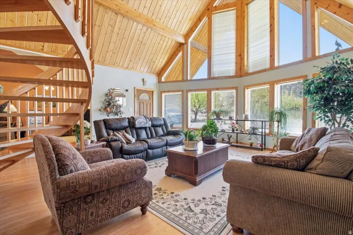 Spacious living area featuring a prominent wood spiral staircase, vaulted wood-plank ceilings, expansive fenestration with transom windows, wood-finish flooring, and light-toned wall finishes