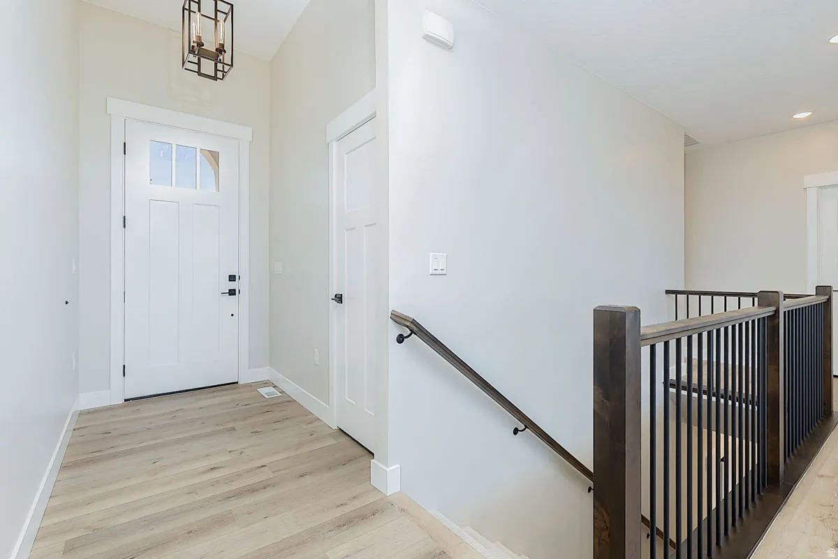 Entryway featuring a white paneled door with glass inserts, wood-finish flooring, a contemporary ceiling light fixture, and a staircase with dark wood newel posts and black metal balusters