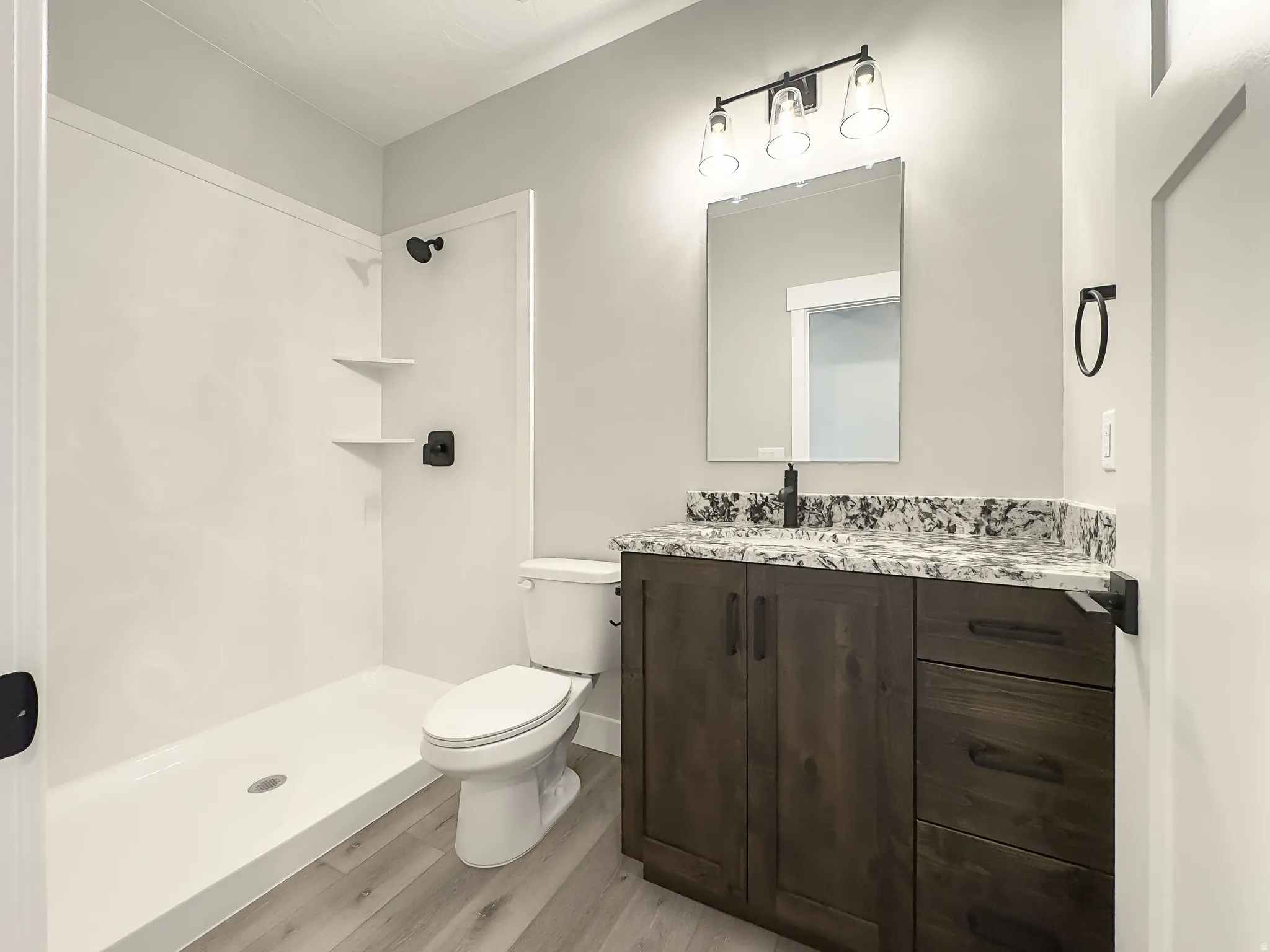 Bathroom featuring a white shower with built-in shelving, a white toilet, and wood-finish flooring