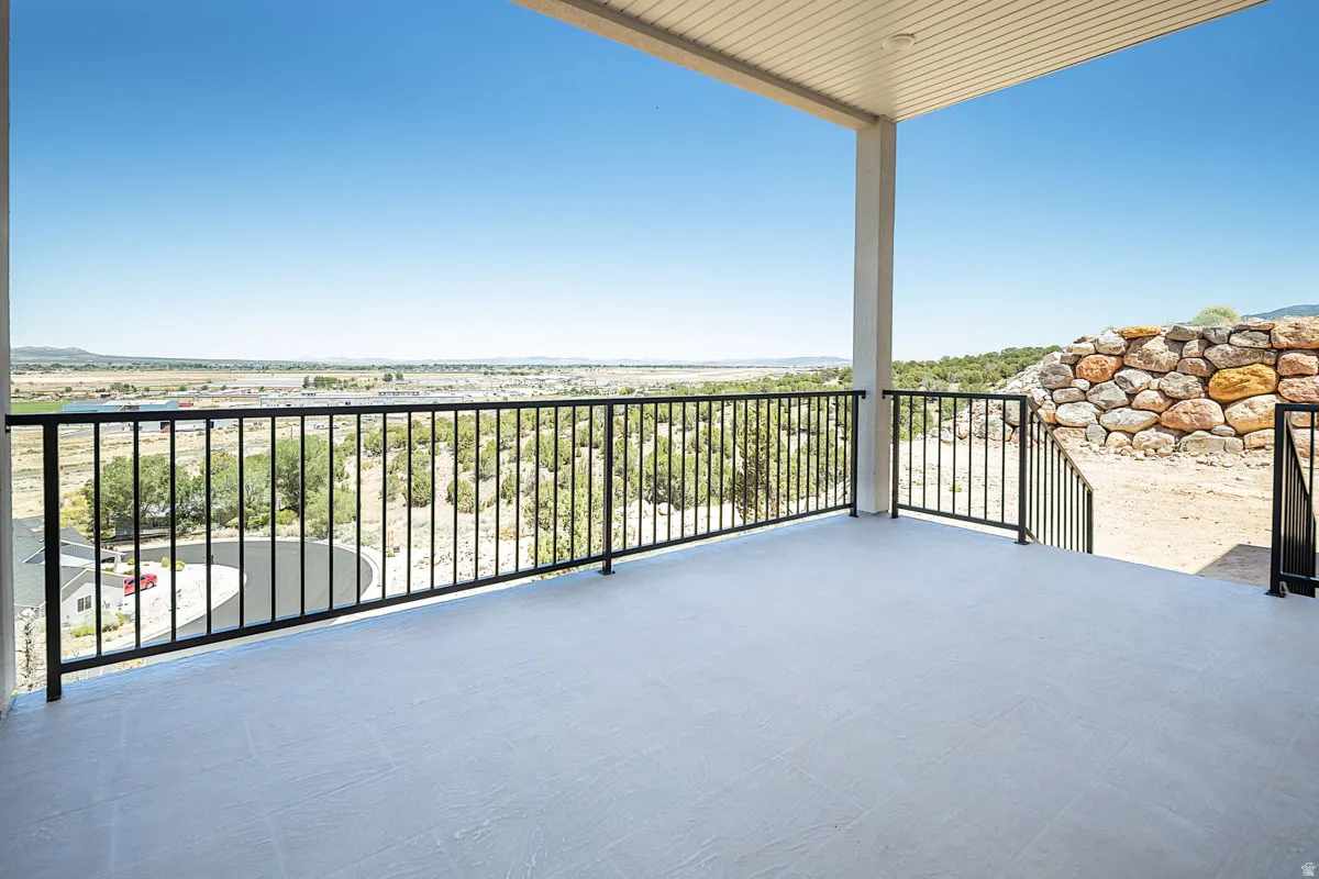 Spacious covered balcony featuring a light-toned concrete surface, black metal railings, and a slatted ceiling