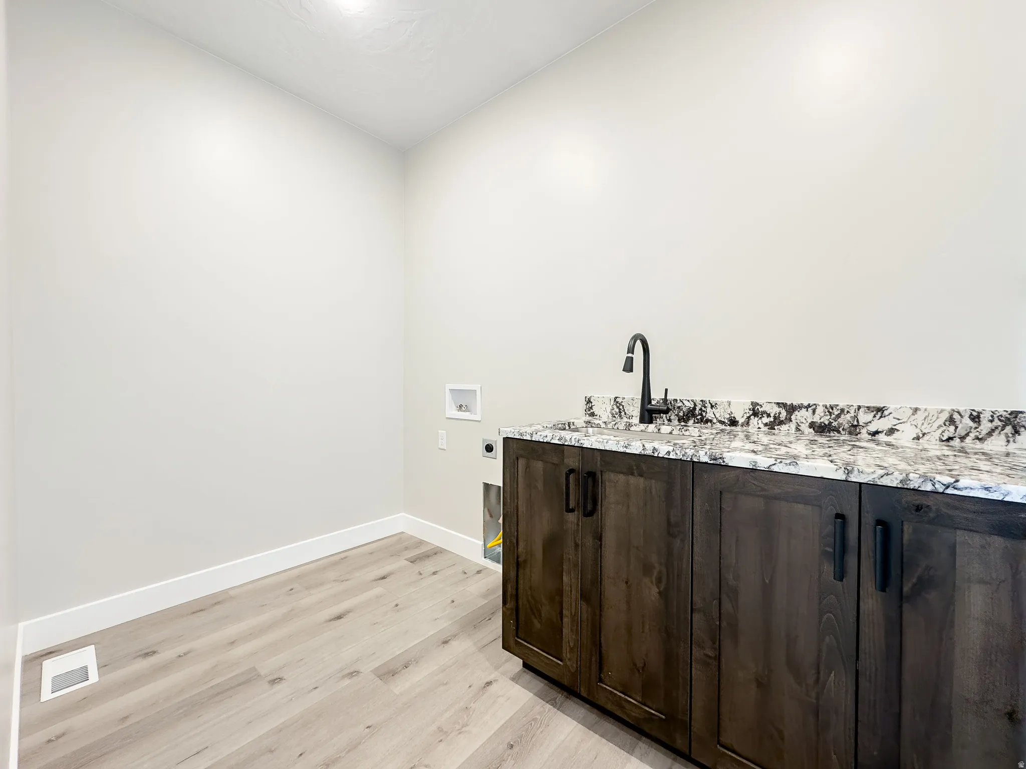 Laundry area featuring wood-finish flooring, light neutral walls, and a recessed ceiling light