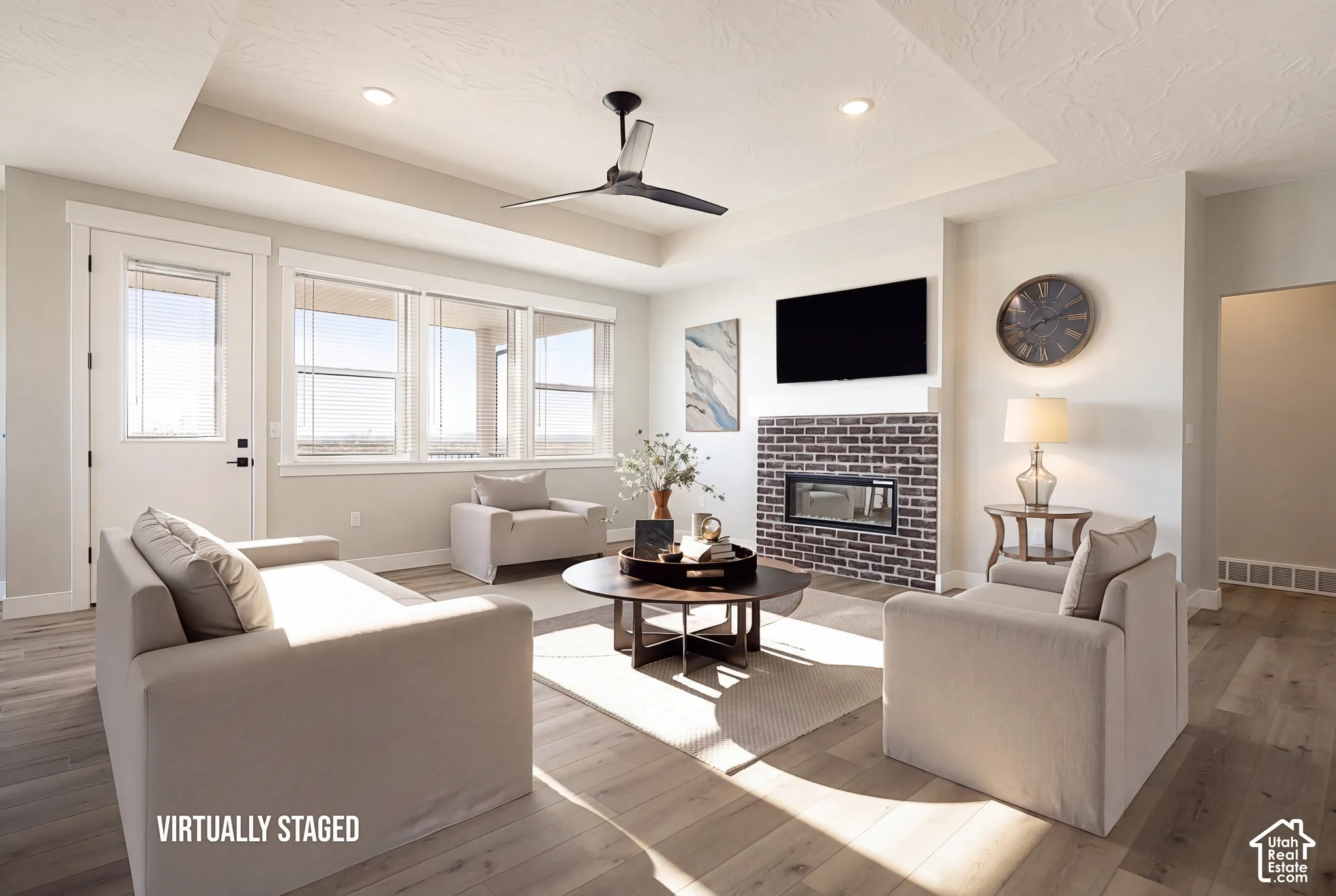 Spacious living area featuring wood-finish flooring, a contemporary ceiling fan, and a fireplace with dark brick surround