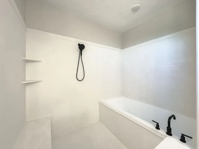 Bathroom featuring a built-in tub with matte black fixtures, a handheld showerhead, and integrated corner shelving