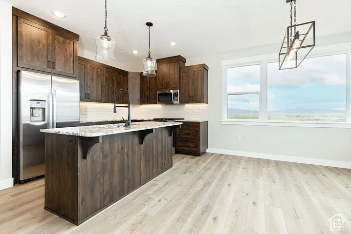 Kitchen featuring stainless steel appliances, dark wood-finish cabinetry, a central island with a light-toned countertop, a tile backsplash, and wood-finish flooring