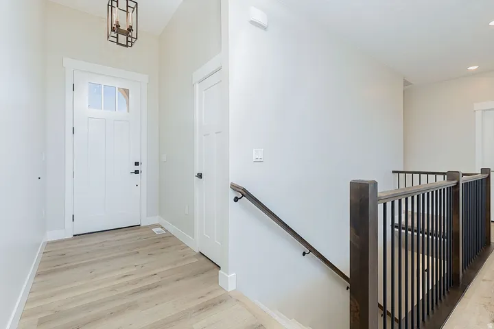 Entryway featuring a white paneled door with glass inserts, wood-finish flooring, a contemporary ceiling light fixture, and a staircase with dark wood newel posts and black metal balusters