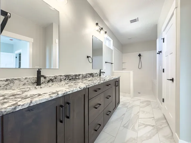Dual vanity with dark wood-finish cabinetry, stone-finish countertops, and matte black fixtures