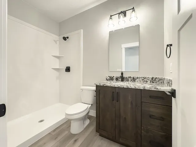 Bathroom featuring a white shower with built-in shelving, a white toilet, and wood-finish flooring
