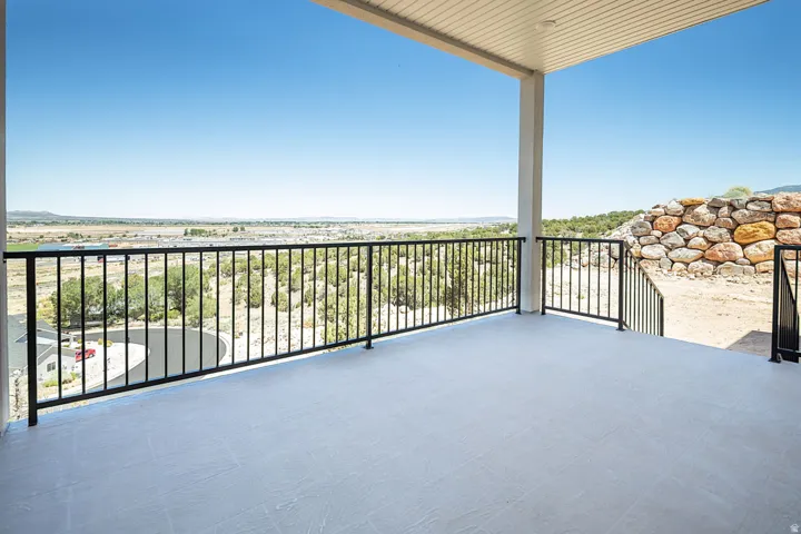 Spacious covered balcony featuring a light-toned concrete surface, black metal railings, and a slatted ceiling